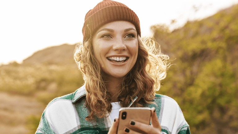 A smiling woman on her phone outside