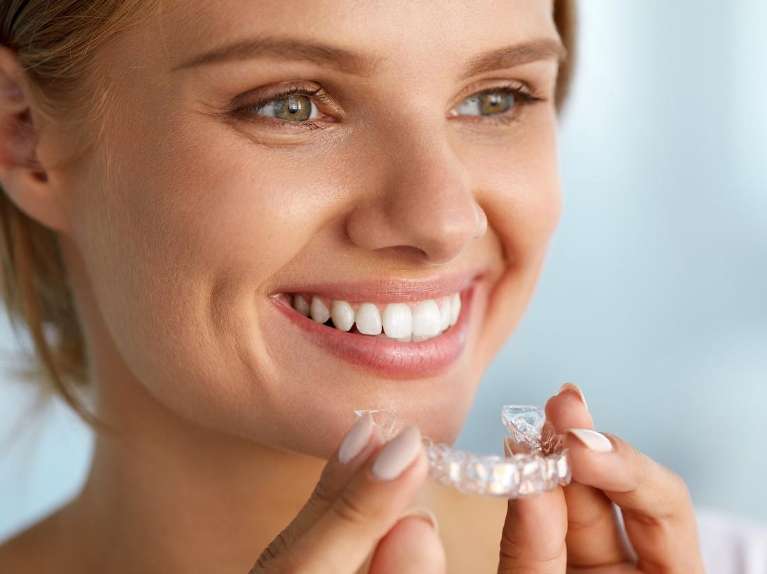 A smiling woman putting in her Invisalign tray