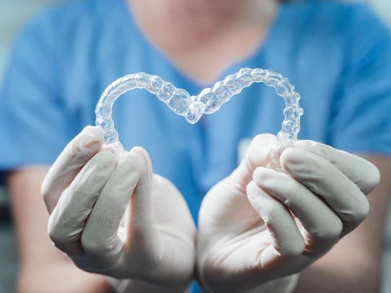 A dentist holding Invisalign trays in the shape of a heart