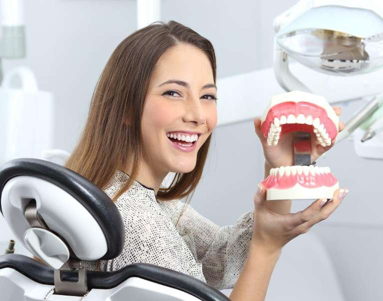 A smiling woman holding a dental model